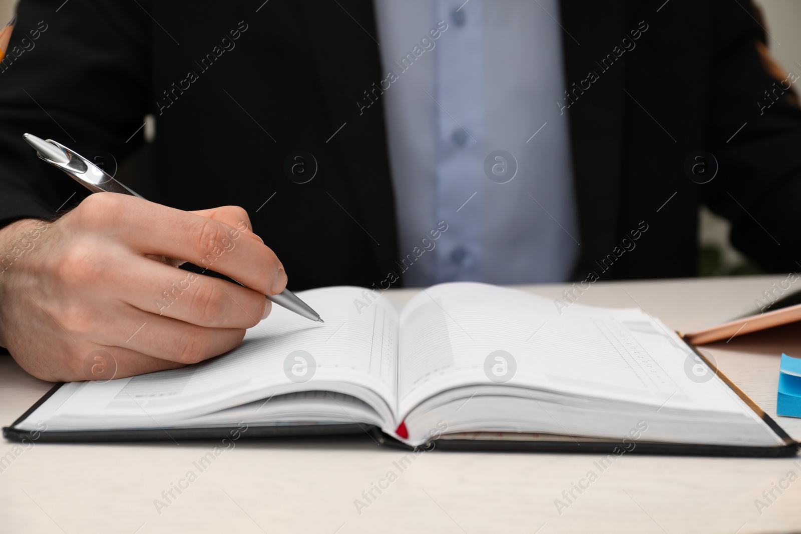 Photo of Man taking notes at white table, closeup