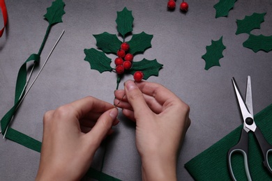 Photo of Woman making mistletoe branch on grey table, top view