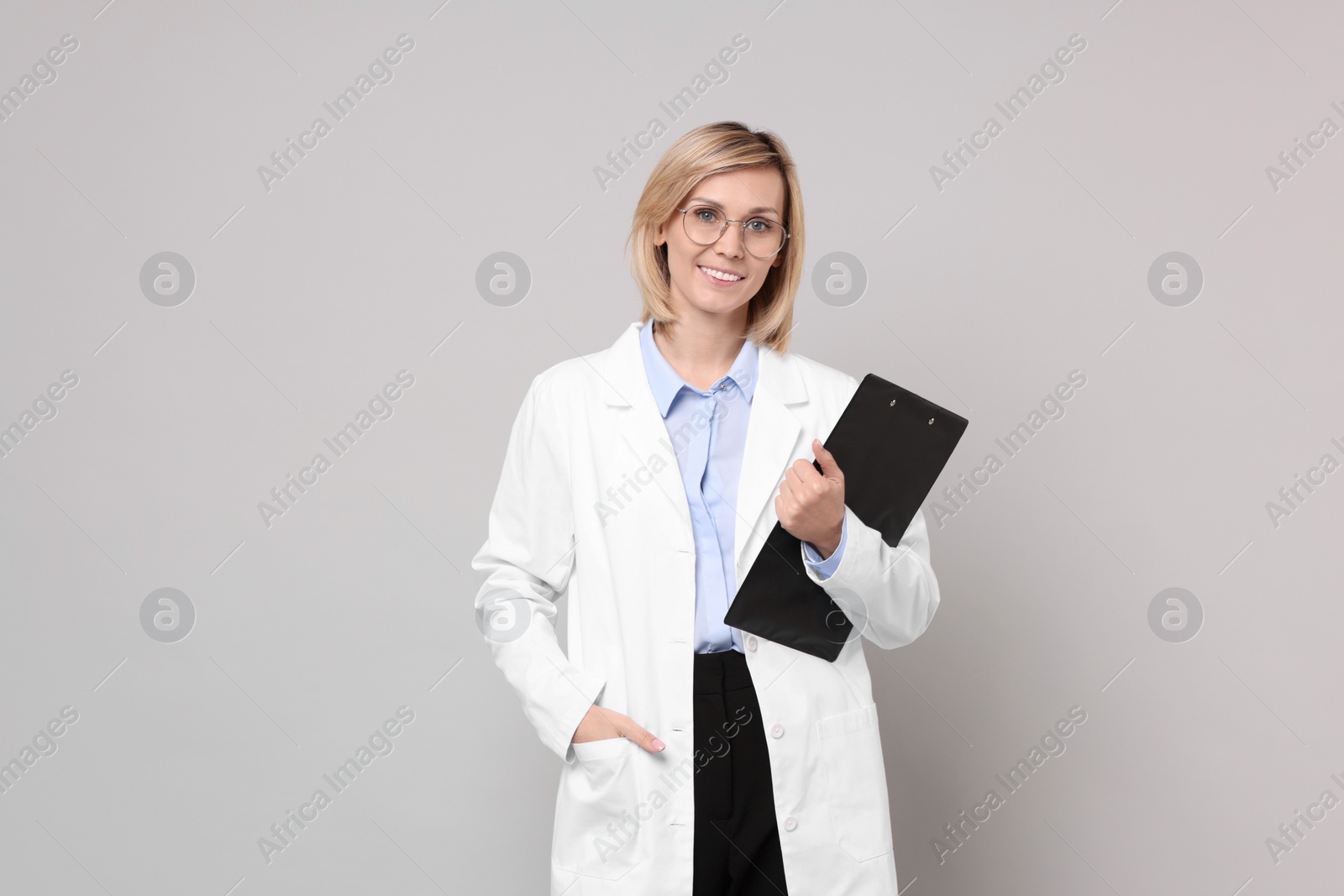 Photo of Smiling doctor with clipboard on grey background