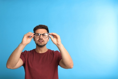 Young man with vision problems wearing glasses on blue background, space for text