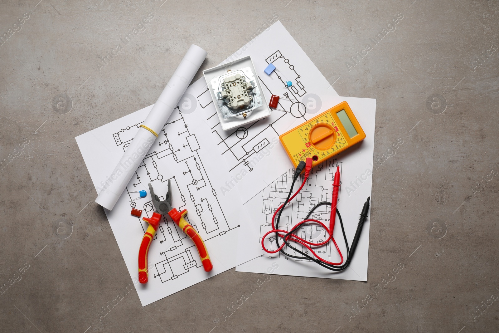 Photo of Wiring diagrams, digital multimeter, pliers, and disassembled light switch on grey table, top view