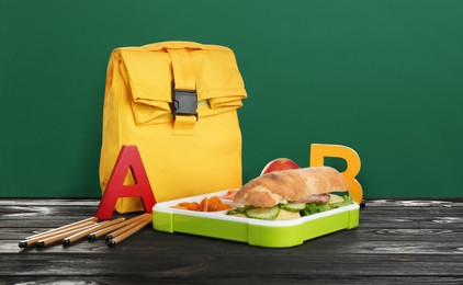 Image of Lunch box with food and backpack on wooden table near green chalkboard