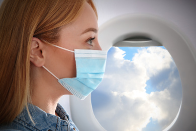 Image of Traveling by airplane during coronavirus pandemic. Woman with face mask near porthole