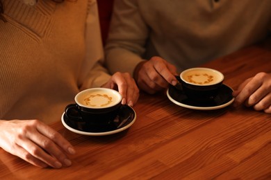 Photo of Couple with cups of aromatic coffee at wooden table, closeup