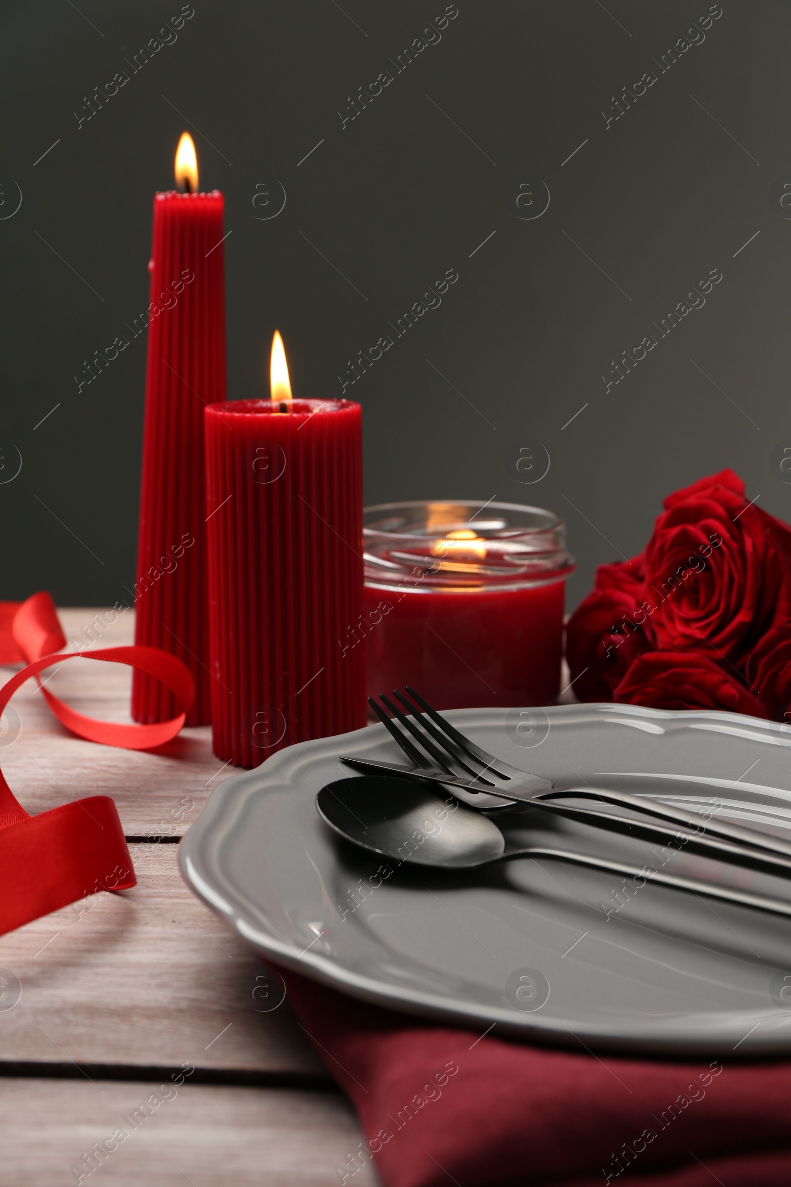 Photo of Romantic place setting with red candles and roses on wooden table, closeup. St. Valentine's day dinner