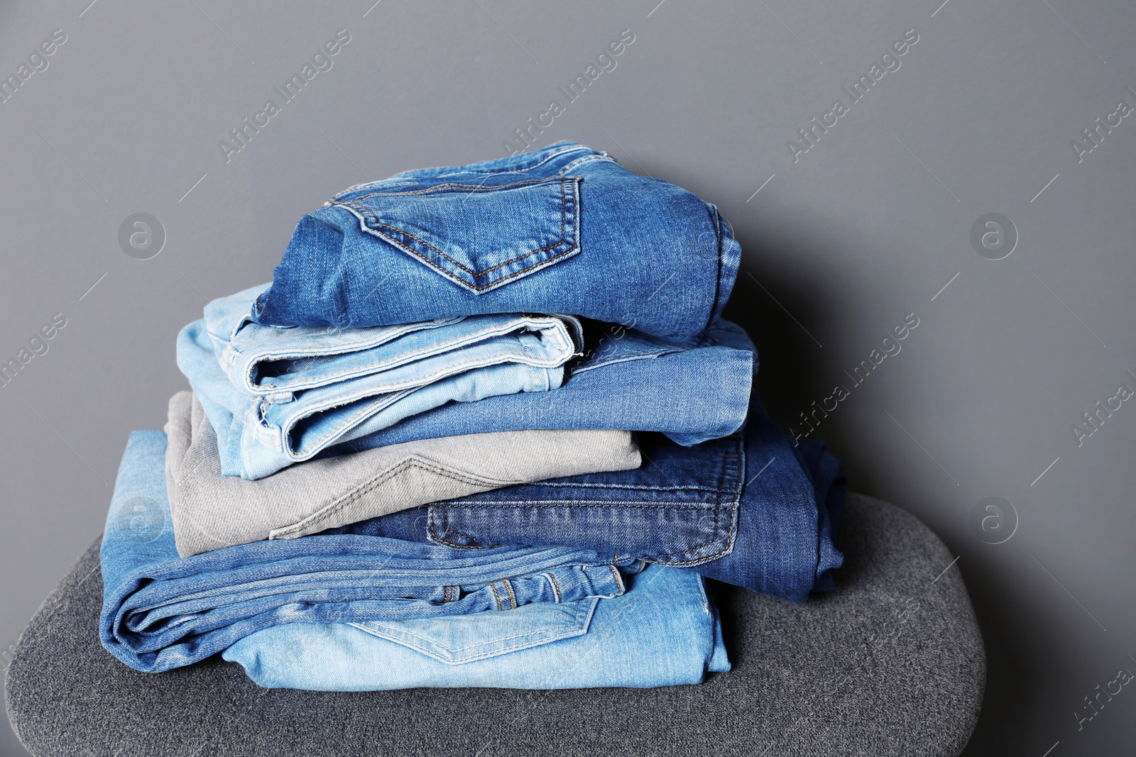 Photo of Stack of different jeans on stool against gray background