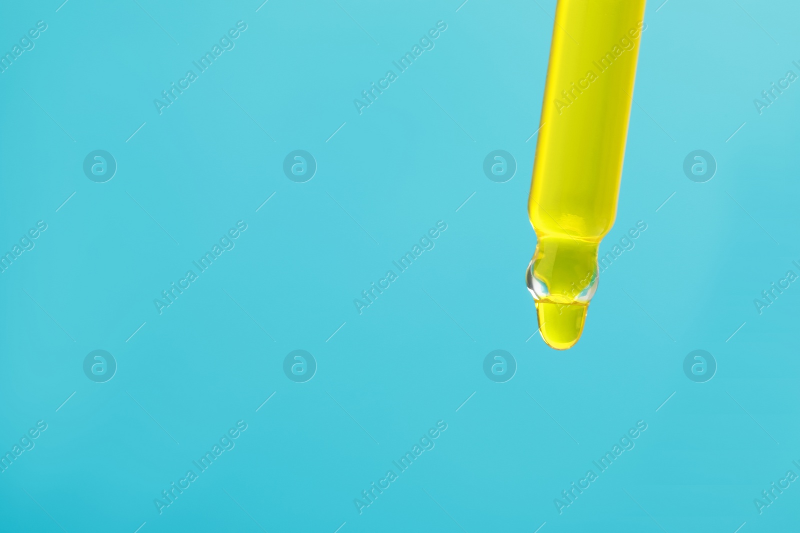 Photo of Dripping yellow serum from pipette on light blue background, closeup. Space for text