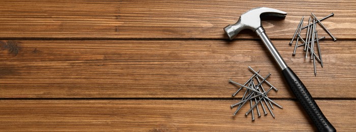 Image of Hammer and metal nails on wooden table, flat lay with space for text. Banner design