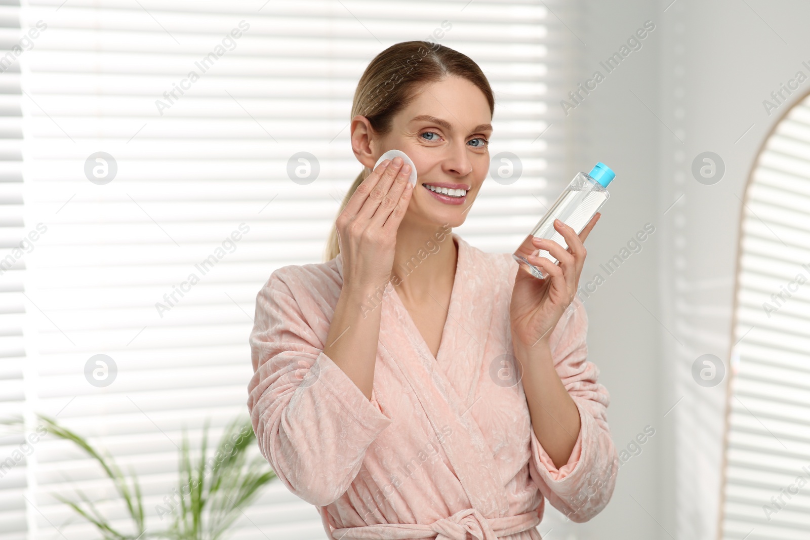 Photo of Beautiful woman removing makeup with cotton pad indoors