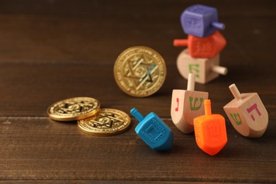 Photo of Dreidels with Jewish letters and coins on wooden table, space for text. Traditional Hanukkah game