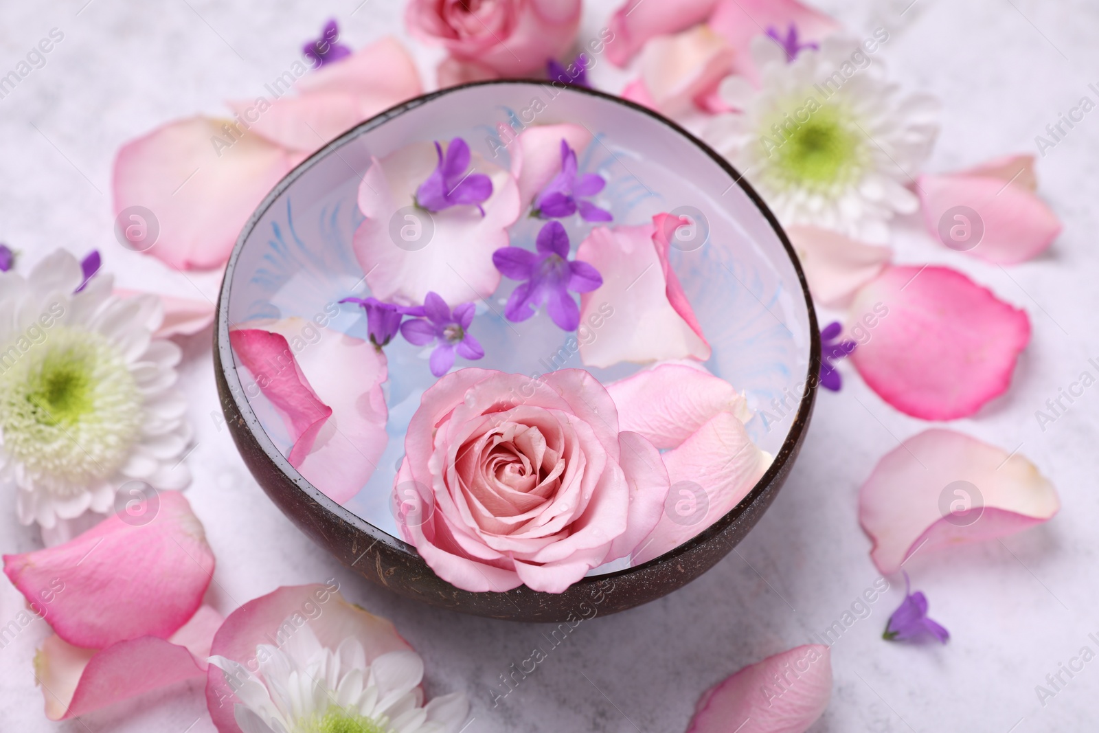 Photo of Beautiful composition with bowl of water and flowers on light table, closeup. Spa treatment