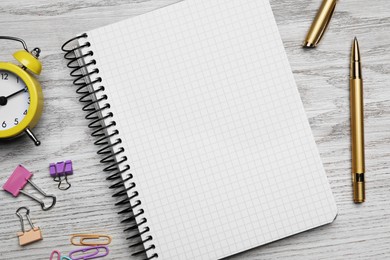 Photo of Ballpoint pen, notebook and different clips on wooden table, flat lay