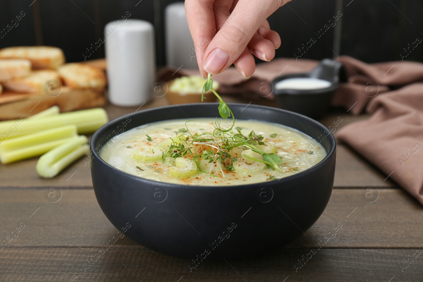 Photo of Woman decorating delicious celery soup at wooden table, closeup