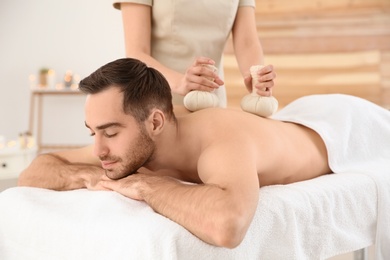 Photo of Handsome man receiving herbal bag massage in spa salon