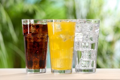 Glasses of different refreshing soda water with ice cubes on white table outdoors