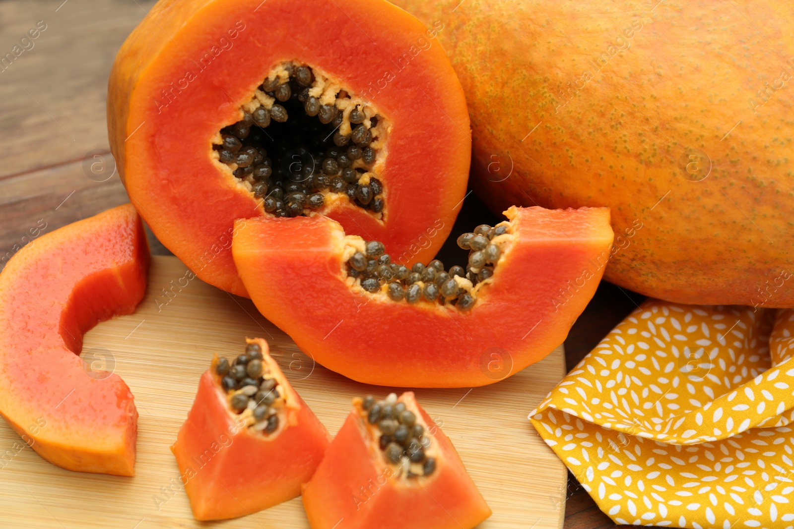 Photo of Ripe cut and whole papaya fruits on wooden table, closeup