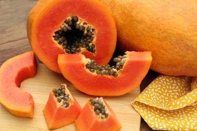 Photo of Ripe cut and whole papaya fruits on wooden table, closeup