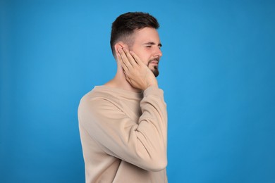 Young man suffering from ear pain on light blue background