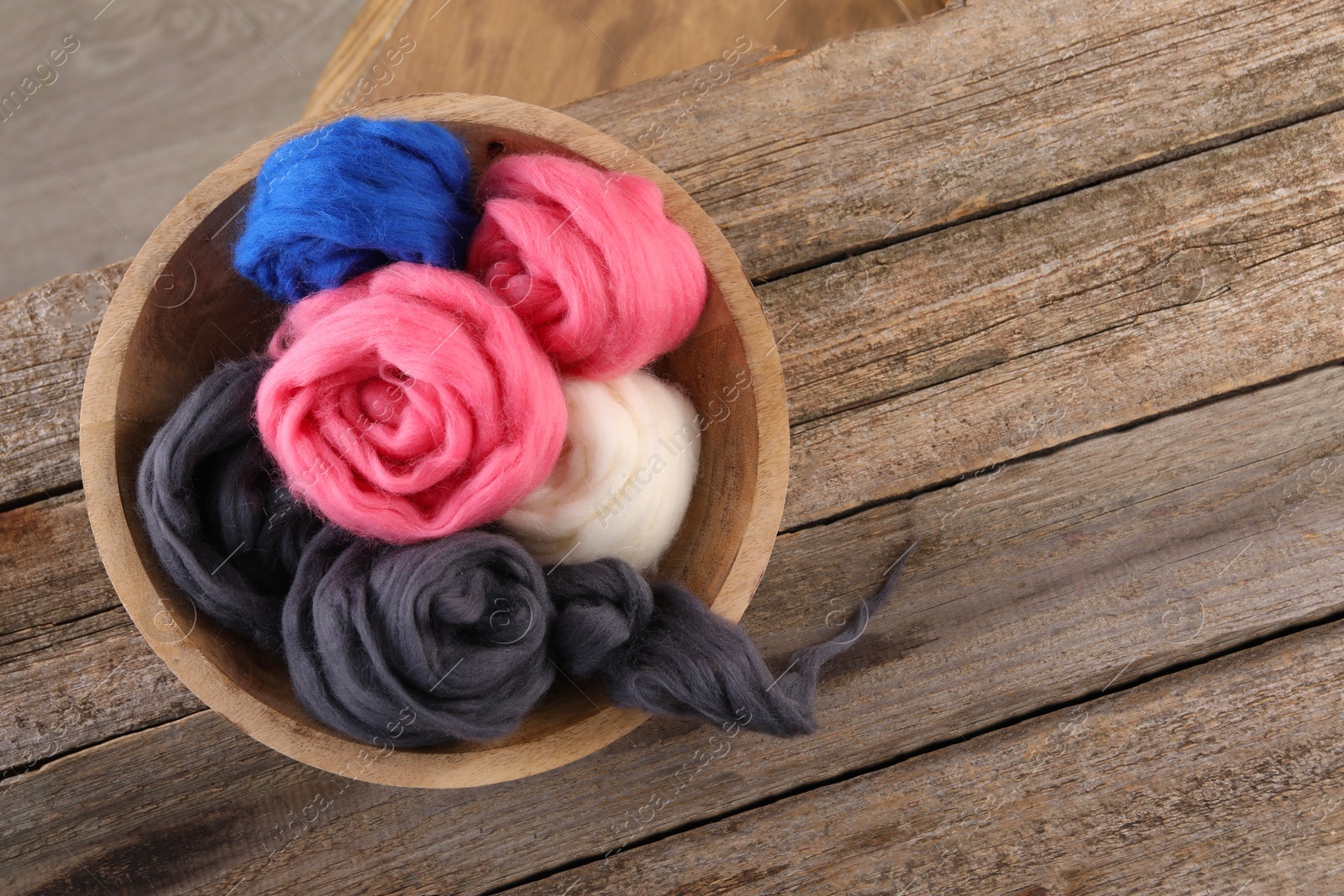 Photo of Colorful felting wool in bowl on wooden table, top view. Space for text