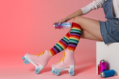 Photo of Woman with vintage roller skates and spray paint cans on color background, closeup