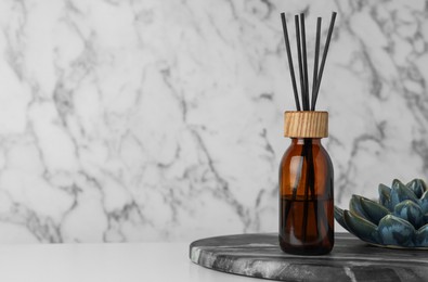 Air reed freshener and ceramic decor on table near marble wall. Space for text