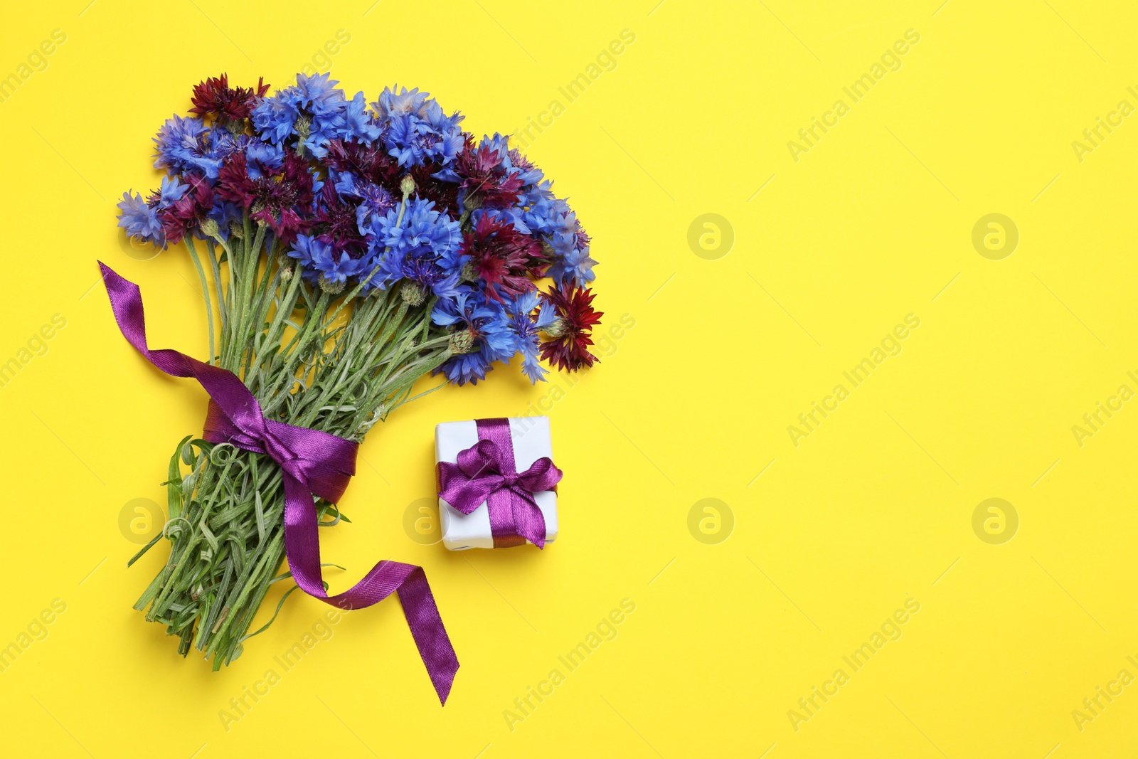 Photo of Bouquet of beautiful colorful cornflowers and gift box on yellow background, flat lay. Space for text