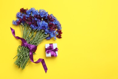 Bouquet of beautiful colorful cornflowers and gift box on yellow background, flat lay. Space for text