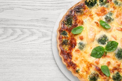 Photo of Delicious homemade quiche with salmon, broccoli and basil leaves on wooden table, top view. Space for text