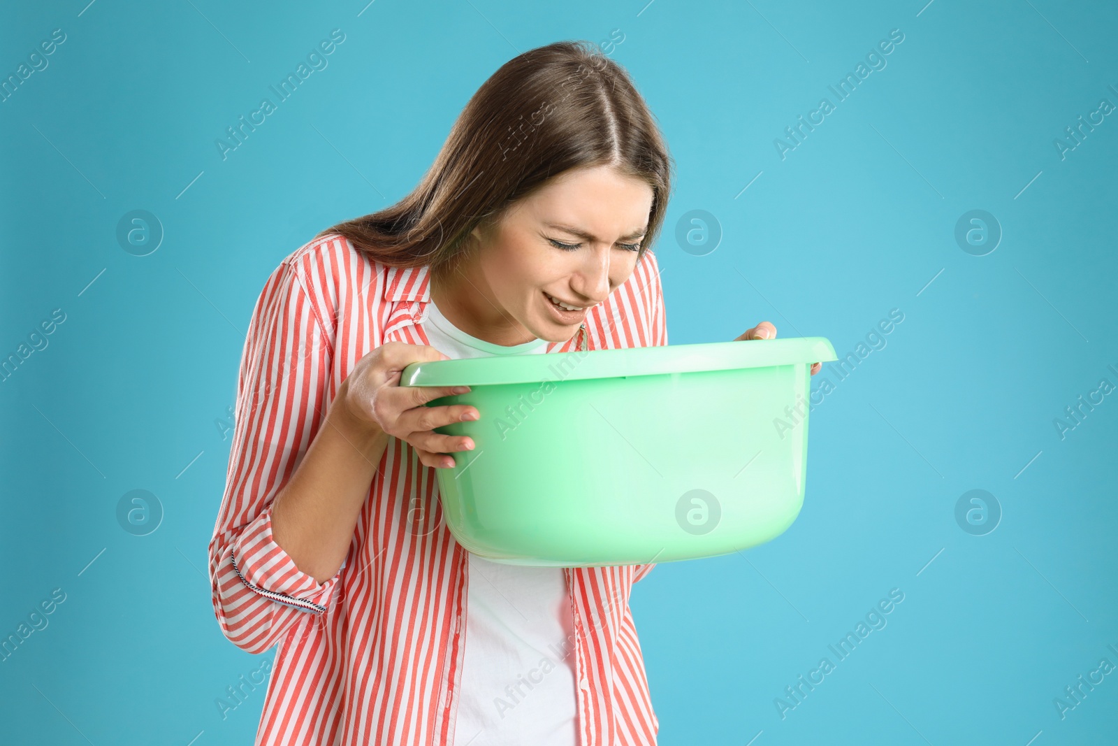 Photo of Woman with basin suffering from nausea on light blue background. Food poisoning