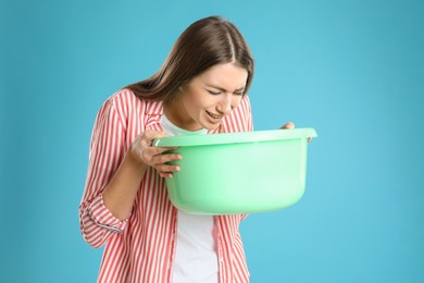 Woman with basin suffering from nausea on light blue background. Food poisoning