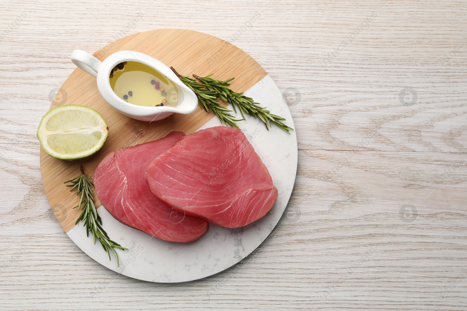 Photo of Raw tuna fillets with rosemary, lime and oil on white wooden table, top view