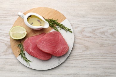 Raw tuna fillets with rosemary, lime and oil on white wooden table, top view