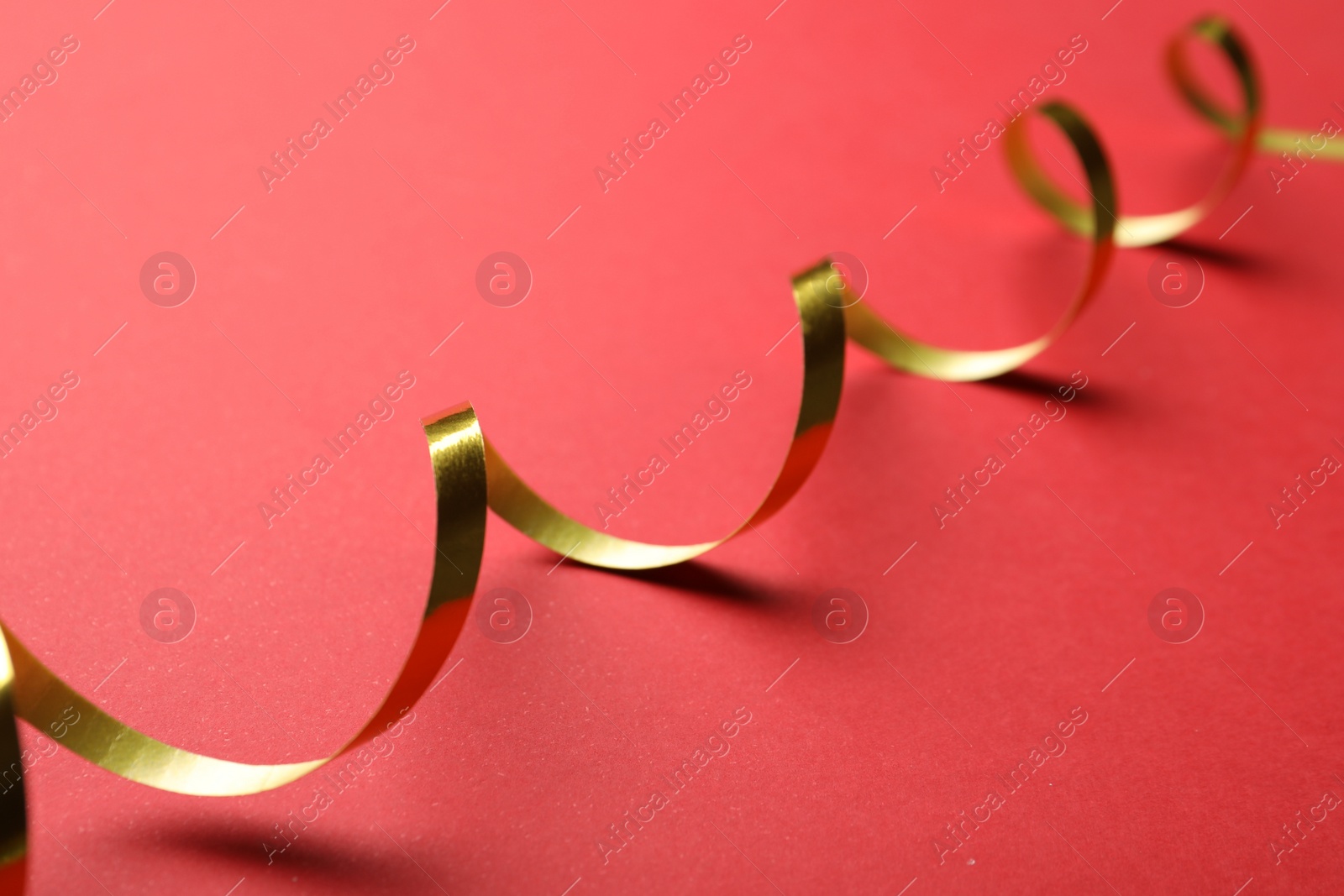 Photo of Shiny golden serpentine streamer on red background, closeup