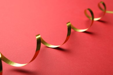 Photo of Shiny golden serpentine streamer on red background, closeup