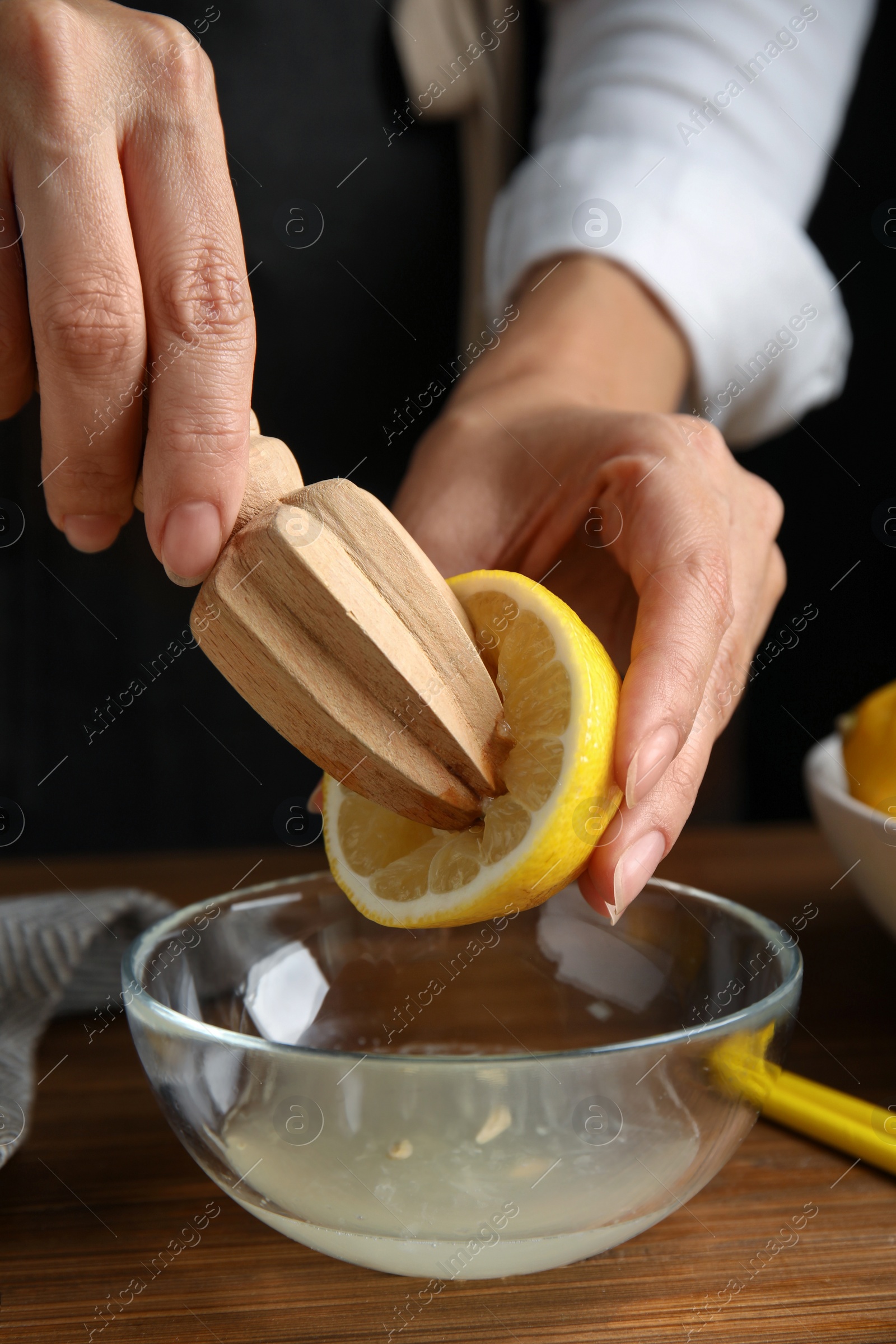 Photo of Woman squeezing lemon juice with citrus reamer at wooden table, closeup