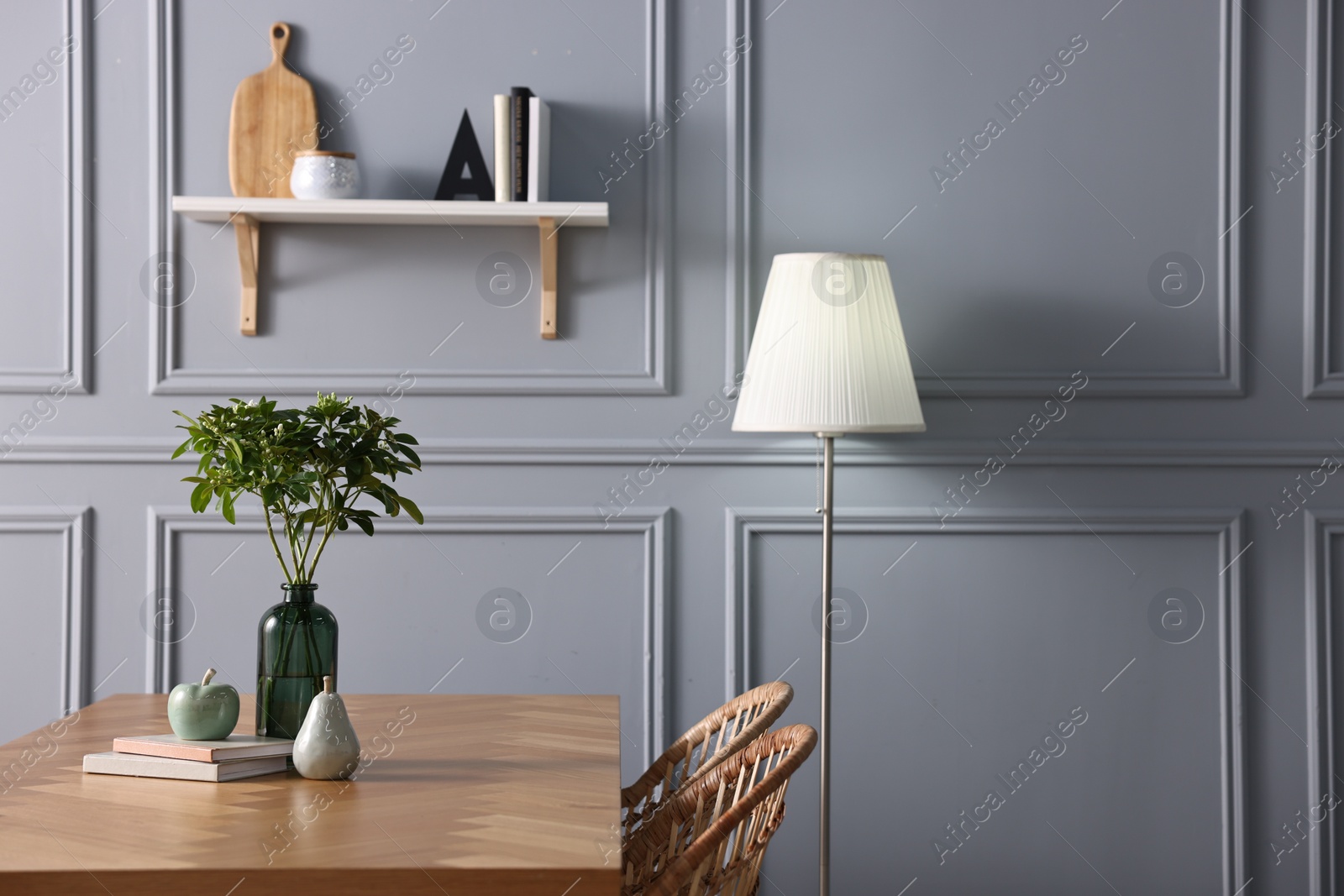 Photo of Vase with green branches, books and decor on wooden table in stylish dining room