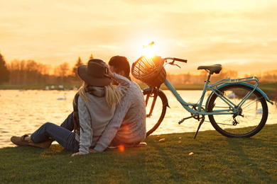 Photo of Young couple near lake at sunset. Perfect place for picnic