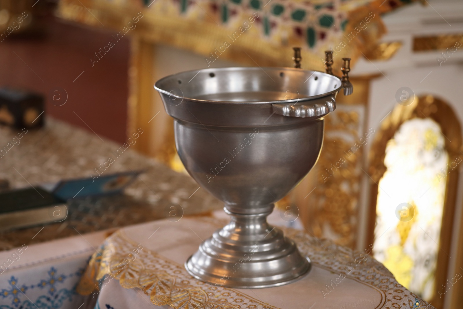 Photo of Silver vessel with holy water on stand in church. Baptism ceremony