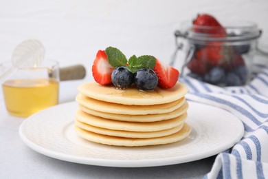 Photo of Delicious pancakes with strawberries, blueberries and honey on light grey table, closeup