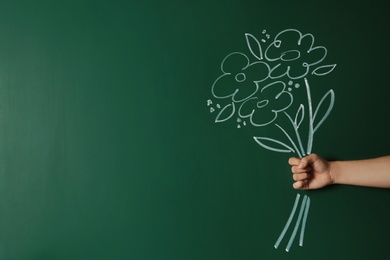 Photo of Closeup view of woman with drawn flowers on green chalkboard, space for text. Teacher's day