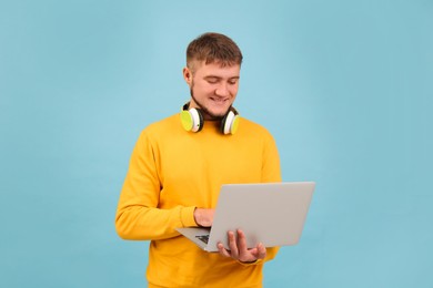Photo of Young student with laptop and headphones on light blue background