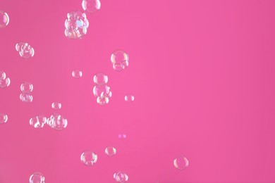 Beautiful transparent soap bubbles on pink background, space for text