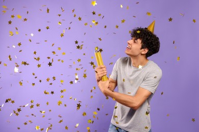 Handsome young man blowing up party popper on violet background