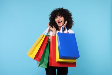 Happy young woman with shopping bags on light blue background