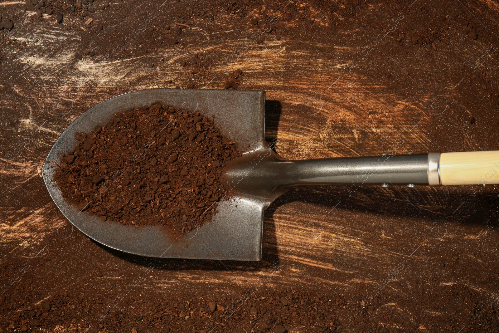 Metal shovel with fertile soil on dirty wooden surface, top view Photo of Metal shovel with fertile soil on dirty wooden surface, top view