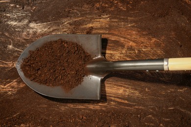 Photo of Metal shovel with fertile soil on dirty wooden surface, top view
