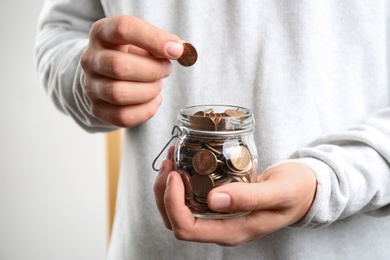 Photo of Man putting coin into glass jar indoors, closeup. Money savings