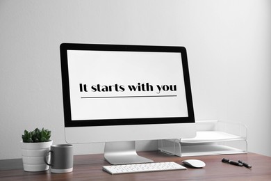 Modern computer with text It starts with you on wooden table