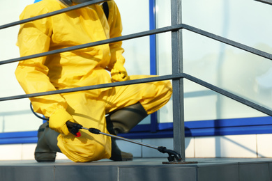 Photo of Male worker in protective suit spraying insecticide on stairs outdoors, closeup. Pest control
