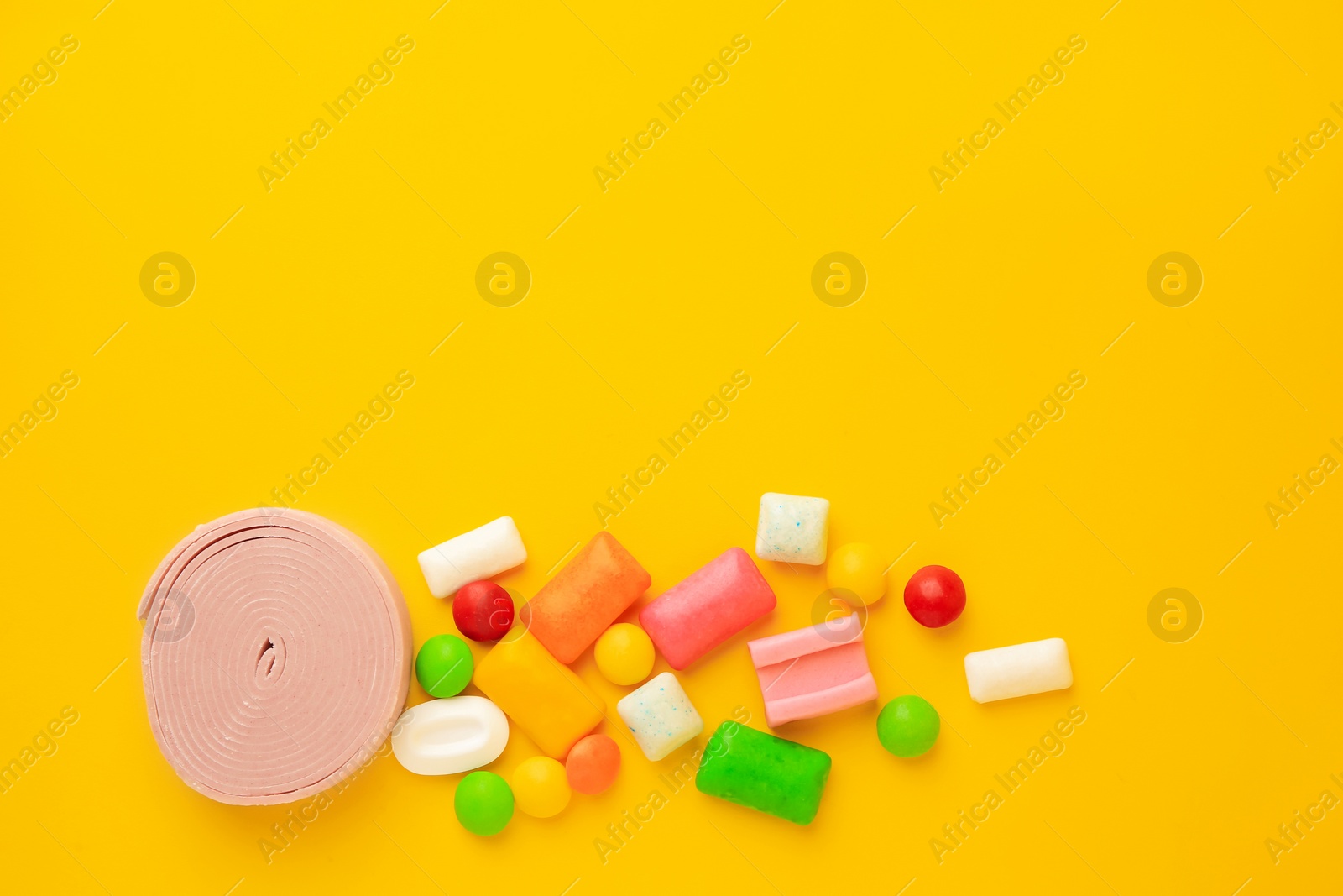 Photo of Many different chewing gums on yellow background, flat lay. Space for text